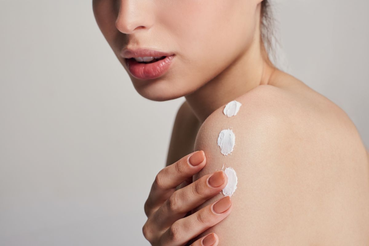 donna che mette la crema corpo sulla spalla 